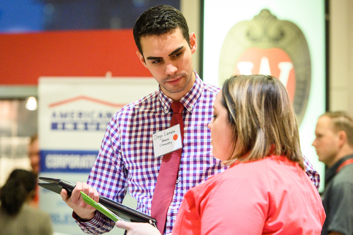 A young woman wearing pink shirt talking with a man recruiter during the career fair.