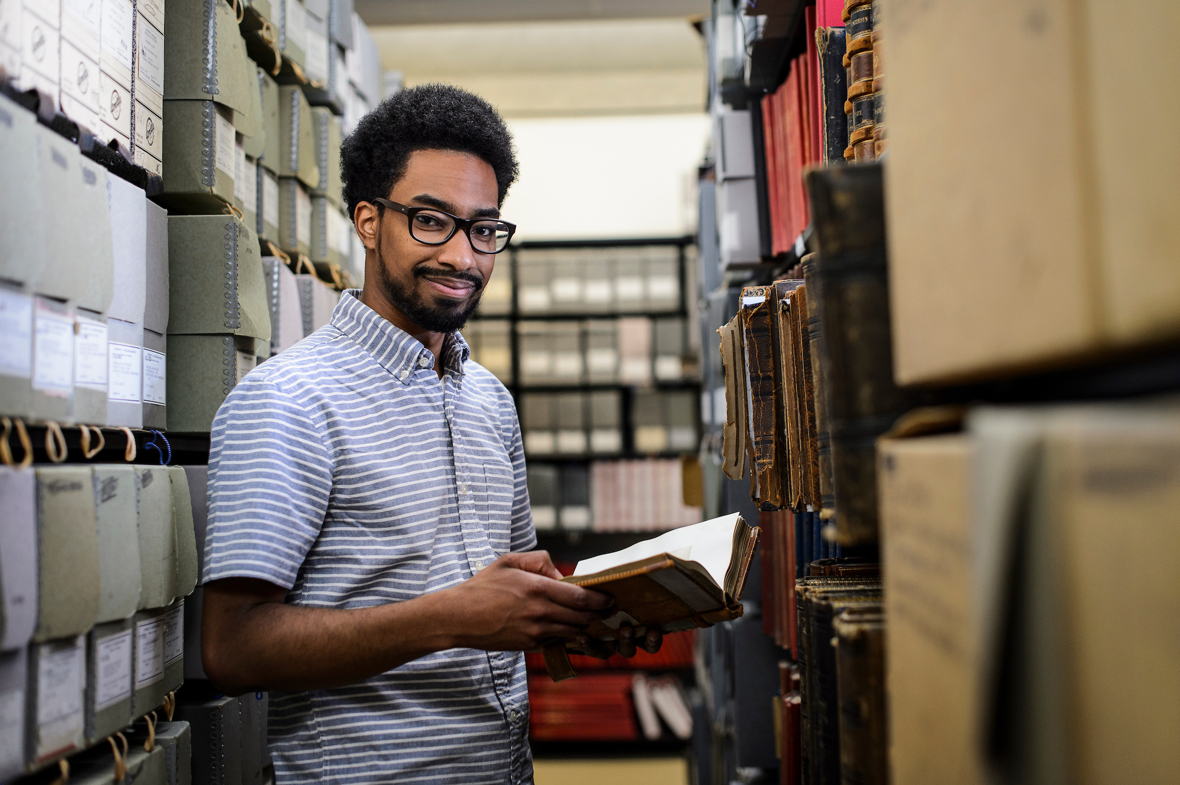 student in library stacks with a book