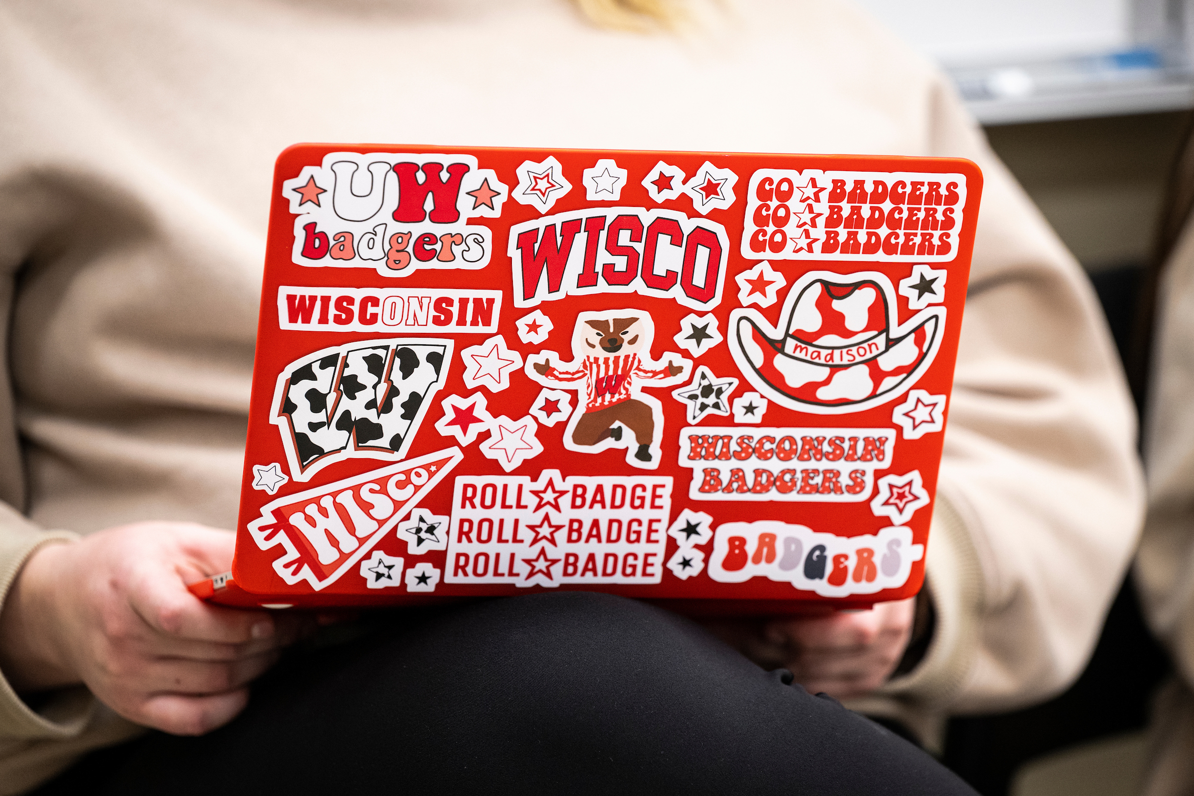 picture of a red lap top covered in UW stickers held by student in cream colors sweatshirt