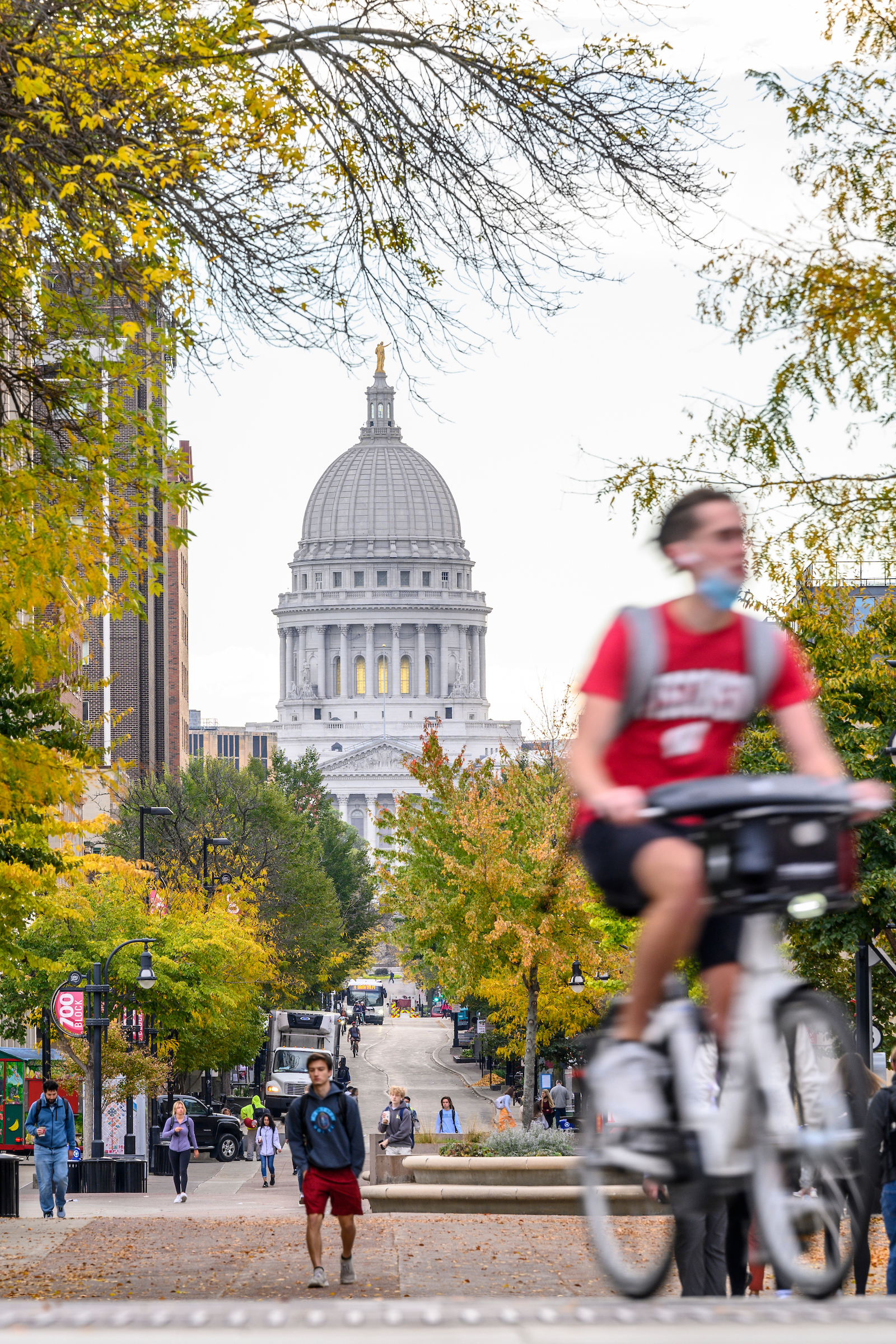 photo of state street with capital and student in Wisconsin t-shirt riding their bike