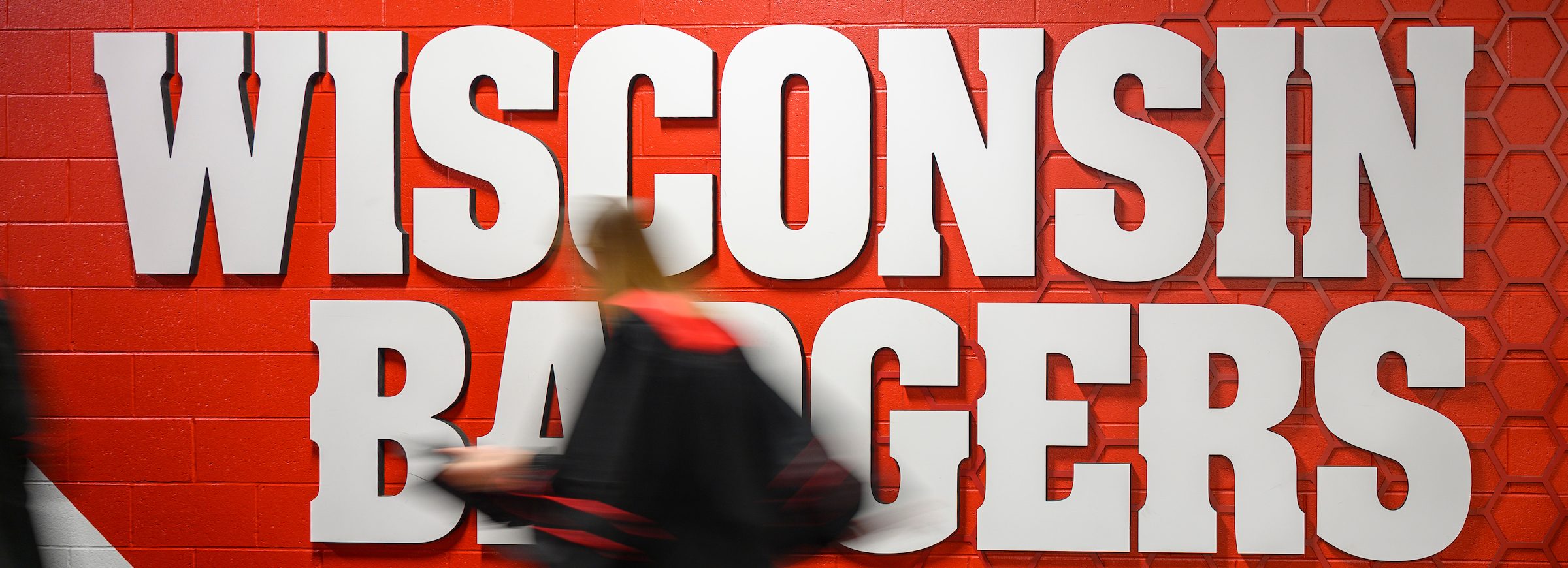 woman running in heels wearing phd garb. running past a wisconsin badgers sign