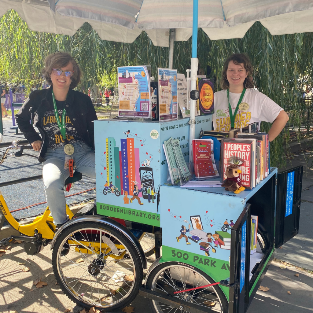 Two women standing on opposite sides of a bike library with books on display