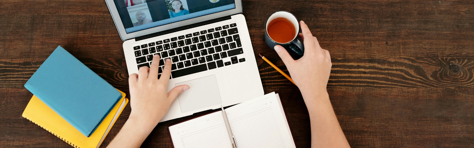 Looking down at someone on a laptop with a coffee and planner. You can only see their forearms and hands.